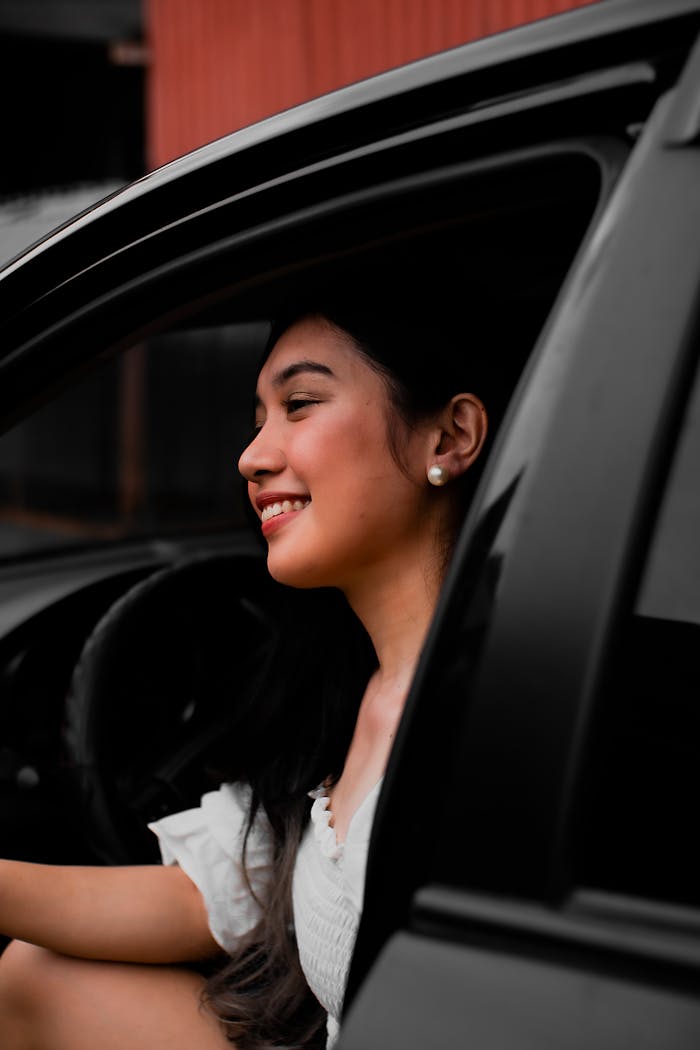 Asian woman smiling while sitting in a car with the door open.