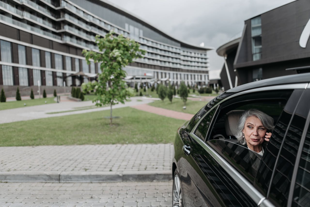 about-02 Elderly woman with grey hair on a phone call sitting in car near modern building.